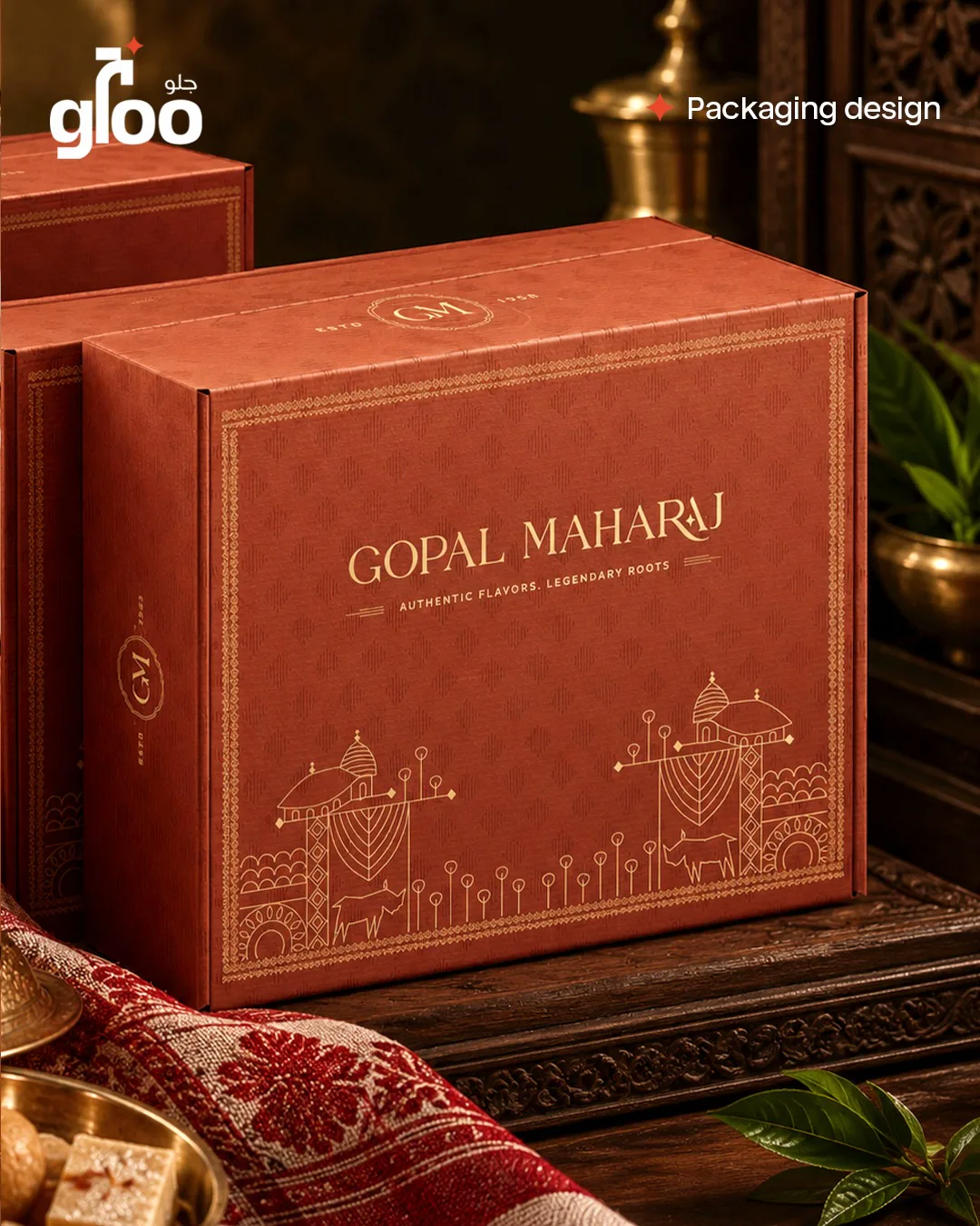 Gopal Maharaj box on a wooden table with a red Assamese gamosa, brass vessels and sweets, warm heritage styling, by The Gloo